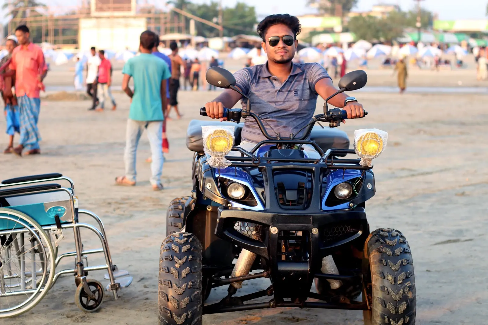 Anik Mahmud independently operating an ATV on a beach, with his wheelchair parked nearby.