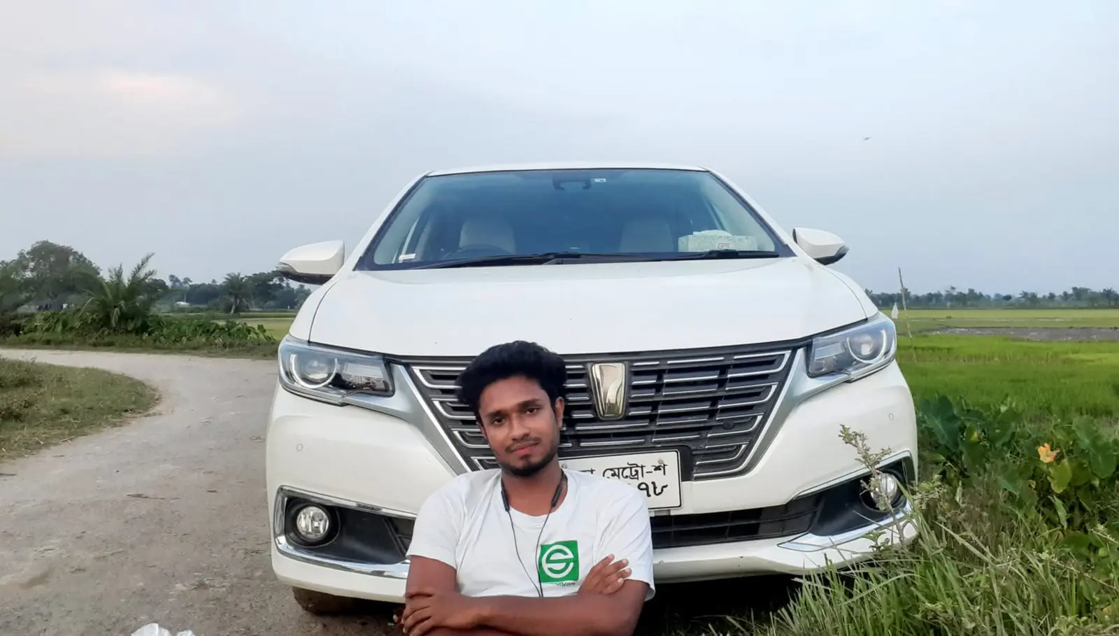Anik Mahmud beside his own car in a field near his village home in 2022, wearing an eShikhon T-shirt.