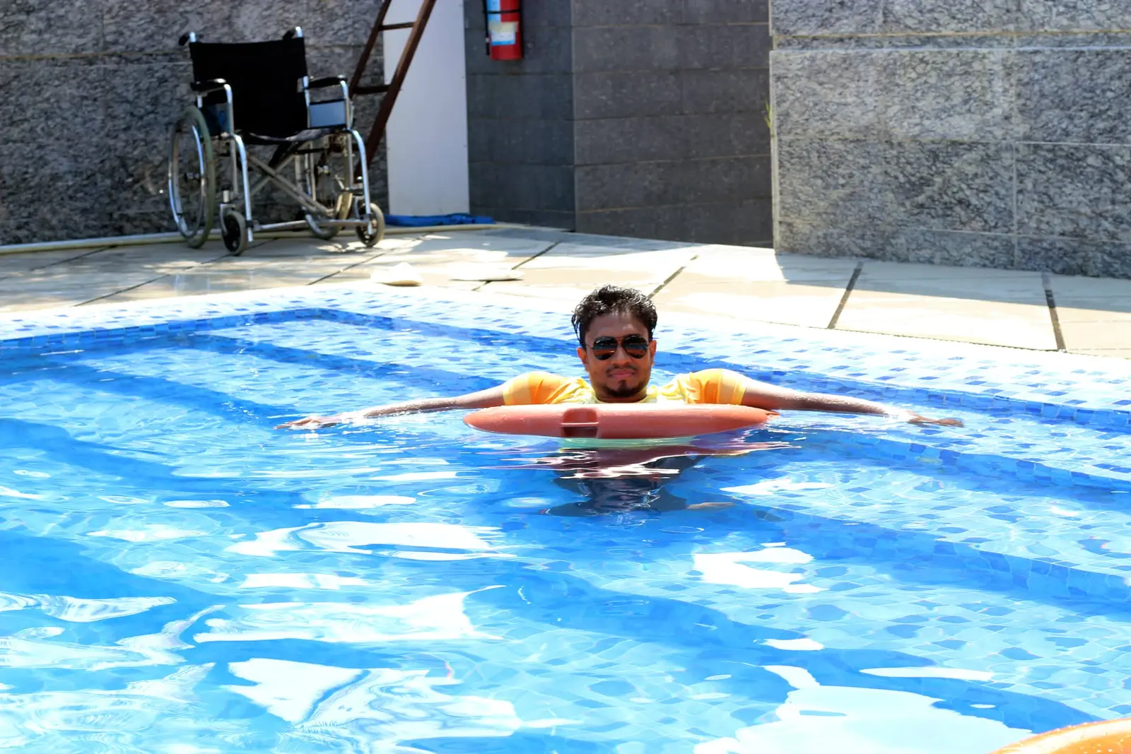 Anik Mahmud relaxing independently in a swimming pool with a flotation ring.