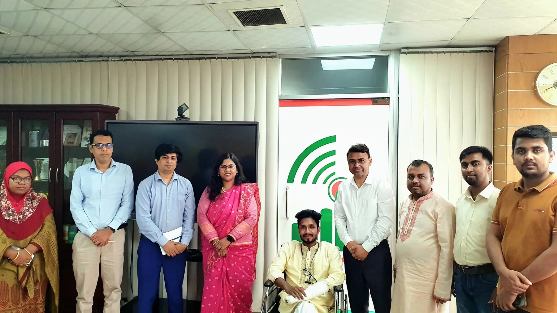 Anik Mahmud in a government meeting room with district officials and Nilufar Yasmin during a 2024 professional discussion.